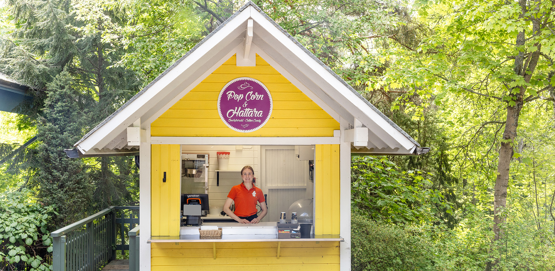 Popcorn ja hattara myyjä iloisena kioskin sisällä.