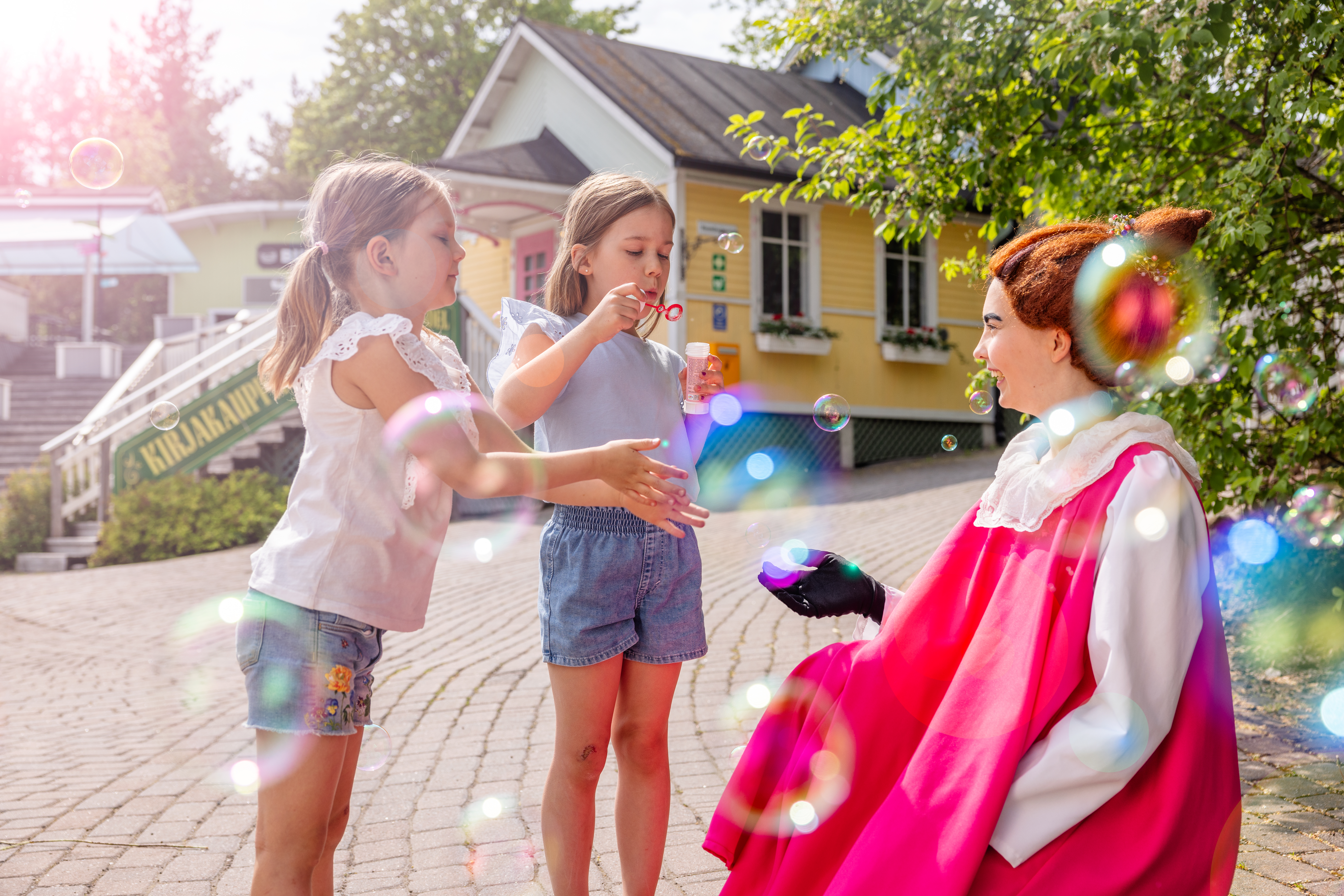 Mymmeli ja lapset puhaltavat saippuakuplia Muumimaailmassa.